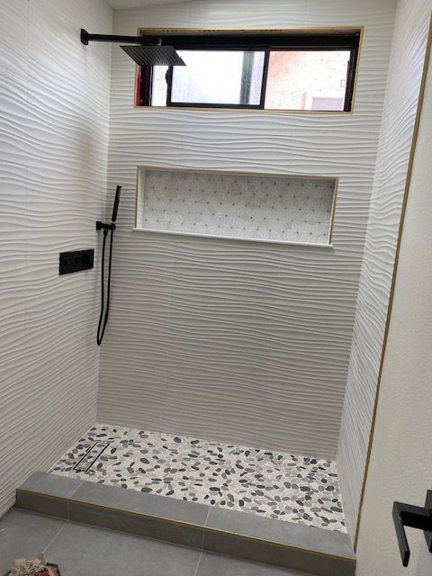 White tiled shower with pebble floor, black fixtures, and a window.