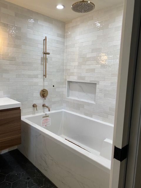 Modern bathroom with white tiled walls, bathtub, and gold fixtures.