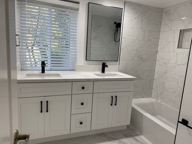White bathroom with double vanity, black fixtures, marble tile, and a bathtub.