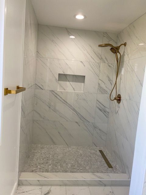 Marble-tiled shower with gold fixtures; recessed shelf; pebble-stone floor.