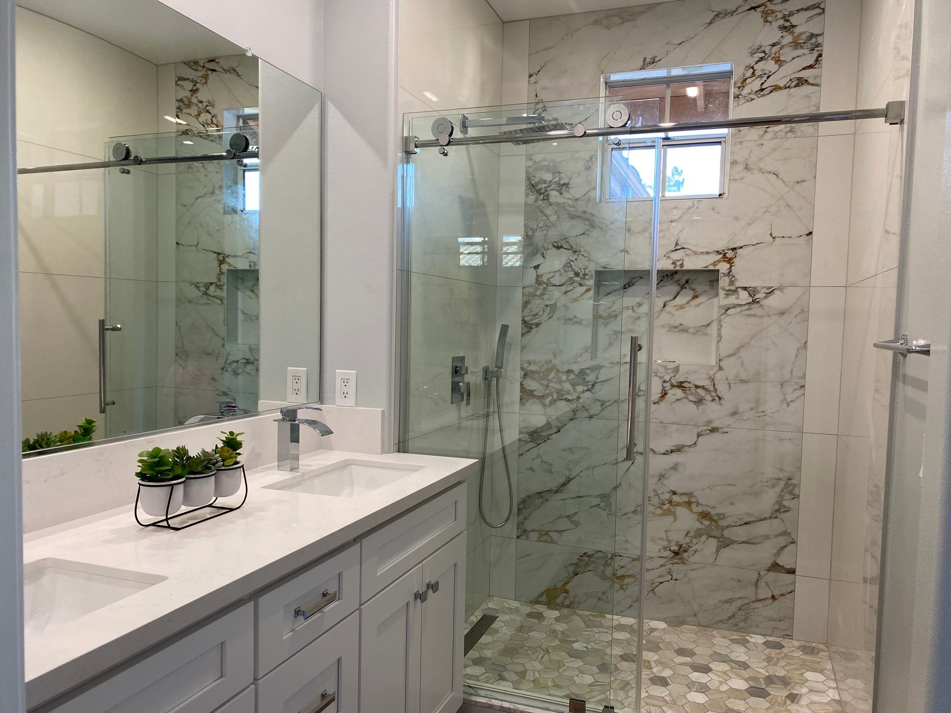 Bathroom with white marble tile, glass shower, double vanity, and a window.