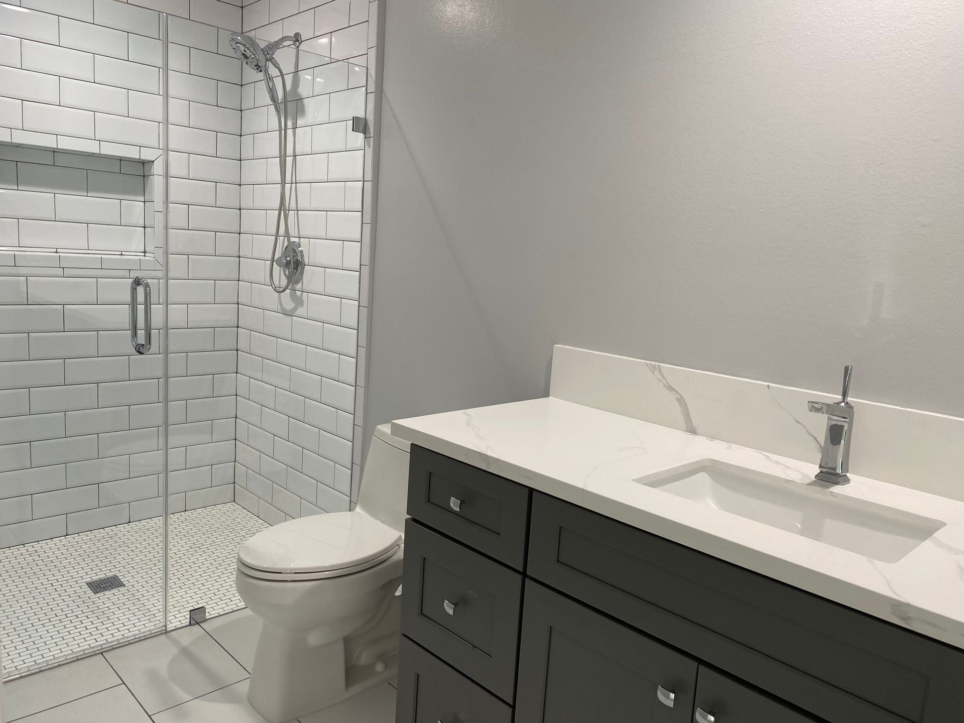 Modern bathroom with white subway tile shower, grey vanity, white countertop, and toilet.