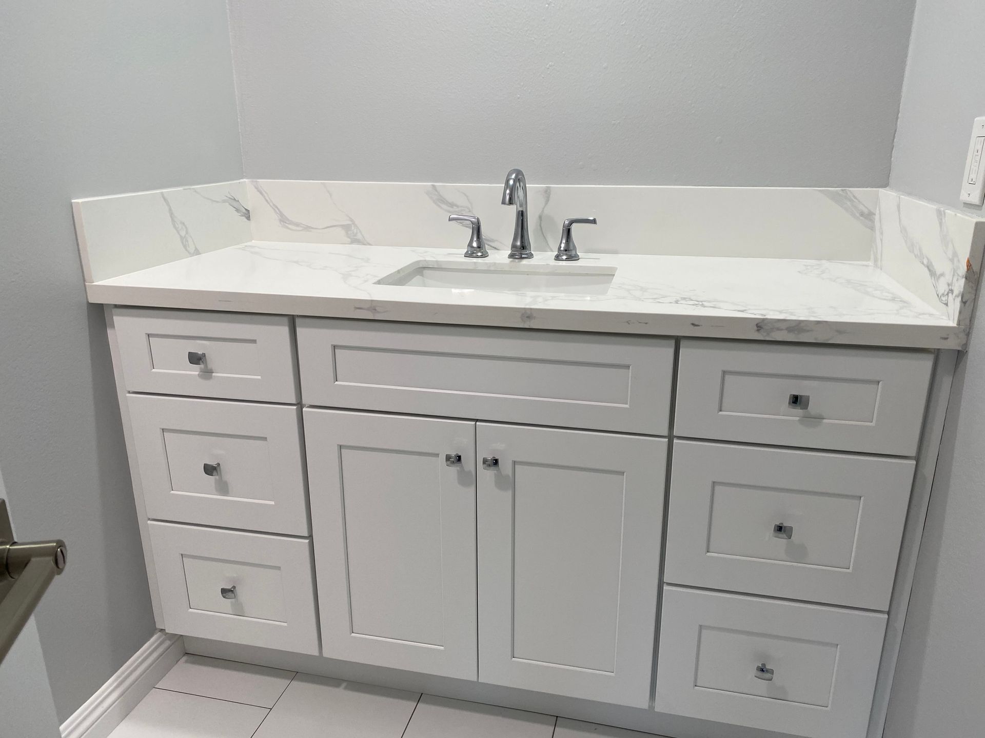 White bathroom vanity with marble countertop and chrome faucet.