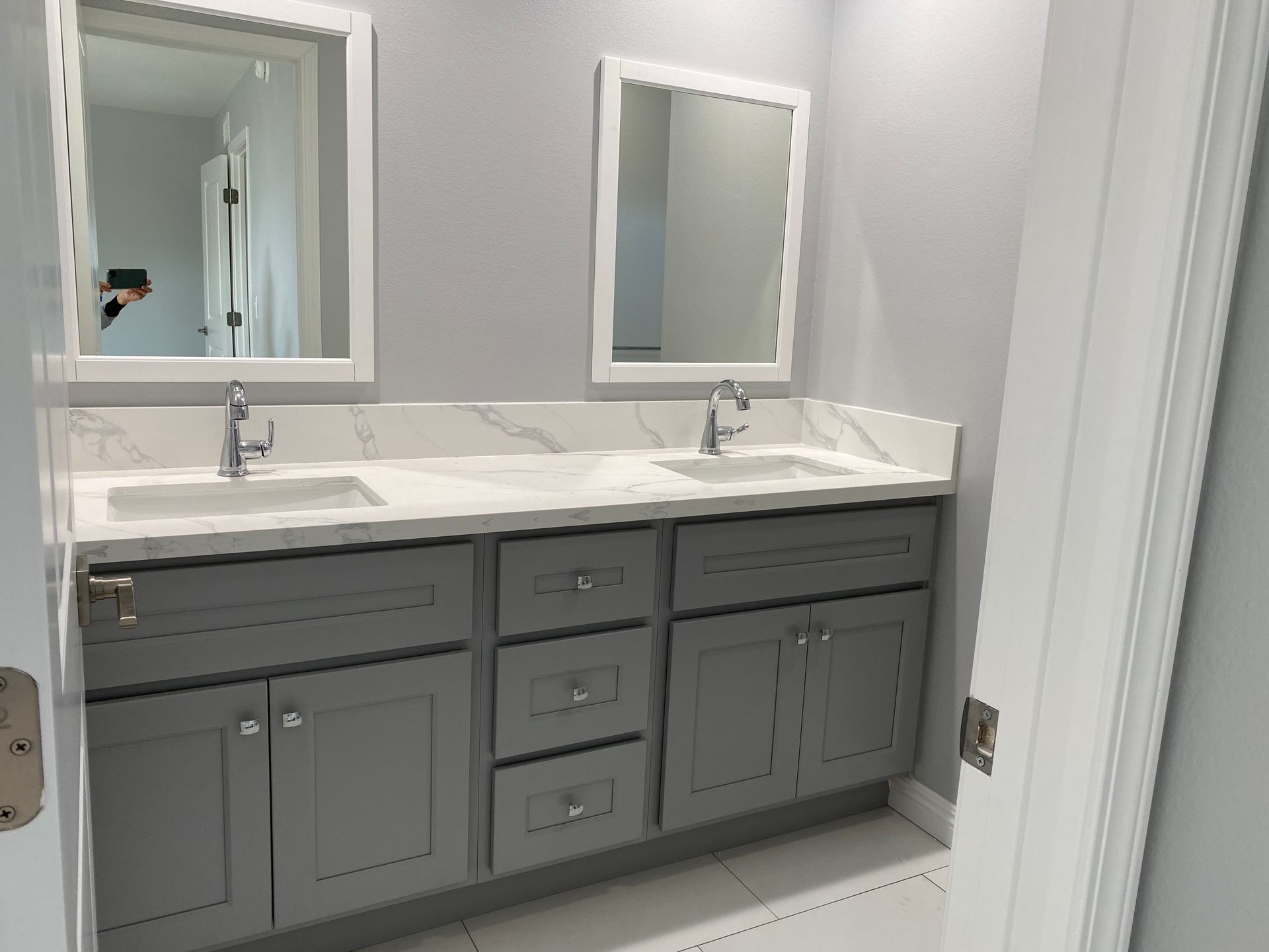 Gray and white bathroom with double sink vanity, mirrors, and door.