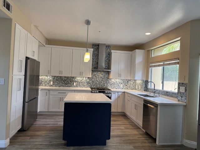 Modern kitchen with white cabinets, blue island, stainless steel appliances, and wood floors.