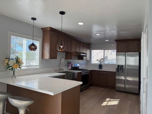 Modern kitchen with brown cabinets, white countertops, stainless steel appliances, and pendant lighting.