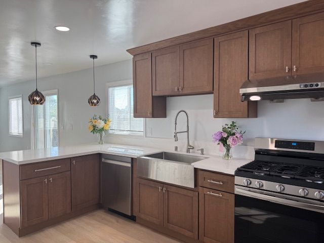 Brown kitchen cabinets, stainless steel appliances, and white countertops. Two pendant lights hang over a light-floored kitchen.