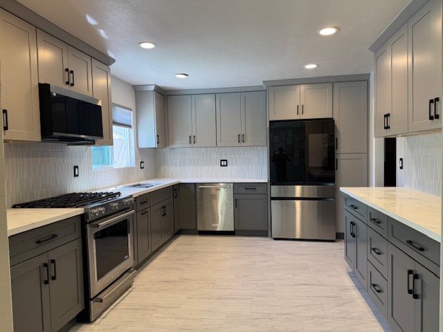 Gray and white kitchen with stainless steel appliances, modern cabinets, and recessed lighting.