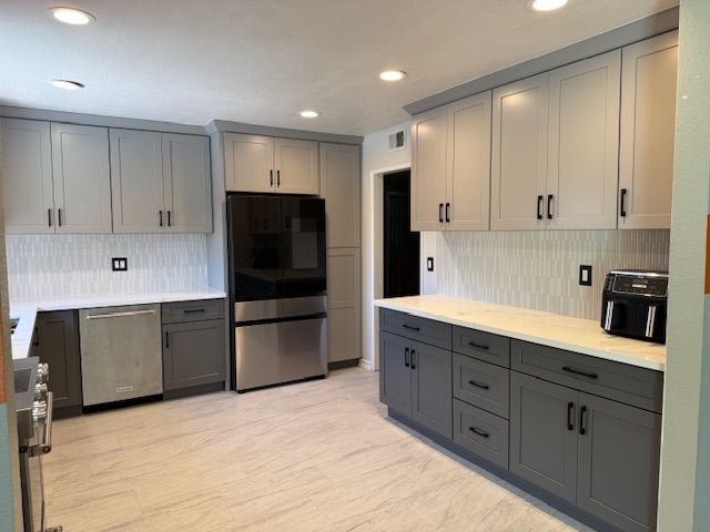 Modern kitchen with gray and white cabinets, stainless steel appliances, and white tile backsplash.