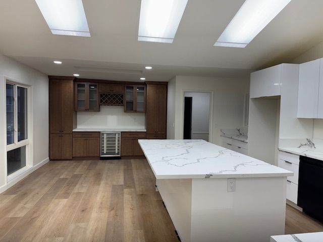 Modern kitchen with white countertops and cabinets, wooden floors, and a dark brown bar area.