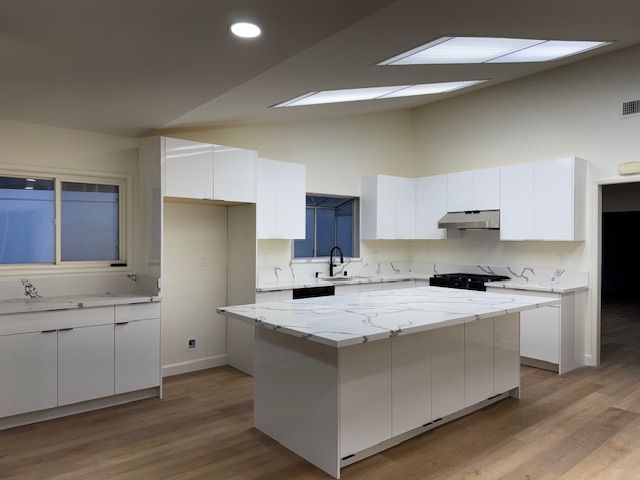 Modern white kitchen with island, marble countertops, stainless steel appliances, and skylights.