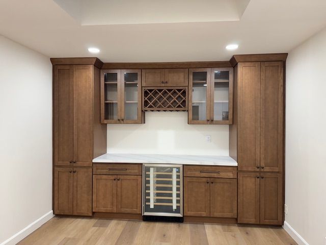 Built-in wooden bar with wine cooler, cabinets, and a wine rack on a white backsplash.