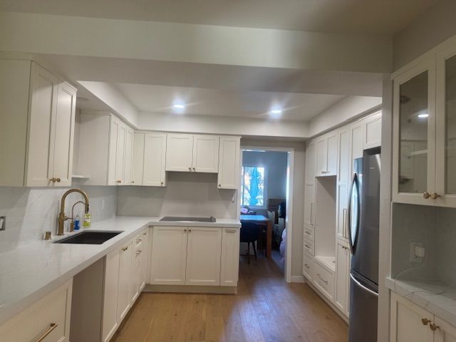 Cream-colored kitchen with light wood floors and countertops. A stainless steel refrigerator is on the right.