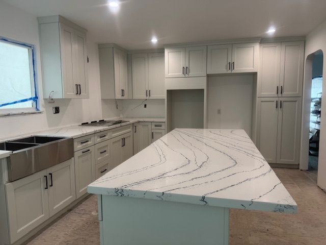 Newly renovated kitchen with light grey cabinets, white countertops, and a large island.
