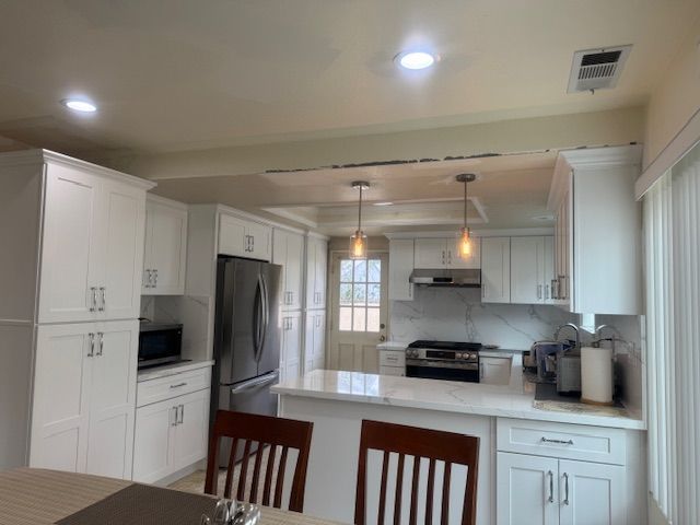 White kitchen with cabinets, stainless steel appliances, and a marble countertop. Two pendant lights hang above the island.