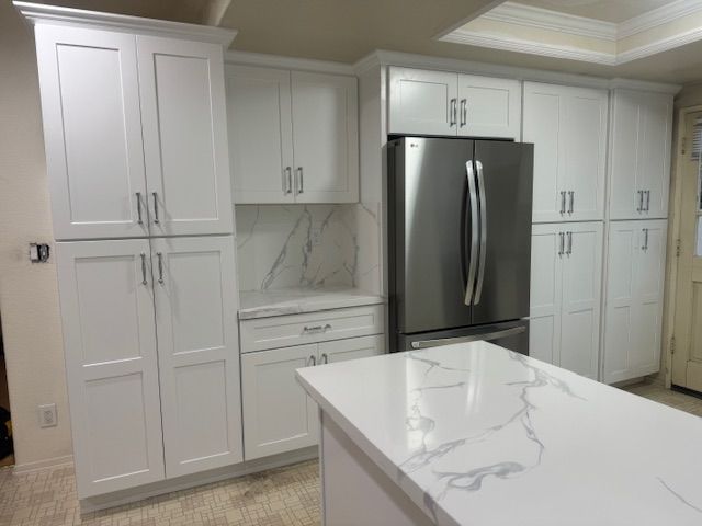 White kitchen with cabinets and a marble countertop island. Stainless steel refrigerator.