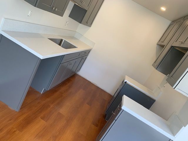 Gray kitchen cabinets with white countertops and wood flooring.