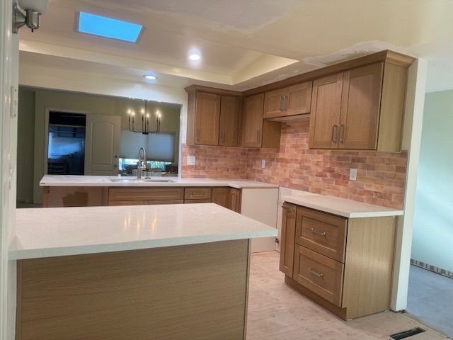 Kitchen with light wood cabinets, white countertops, and brick backsplash.