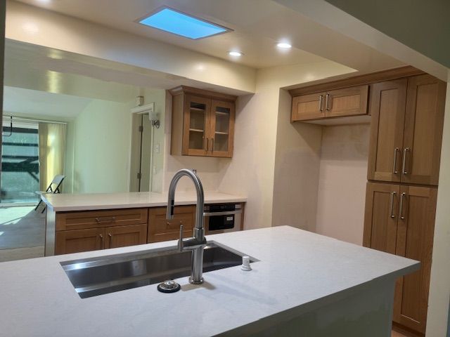 Modern kitchen with light wood cabinets, white countertops, and a stainless steel sink.