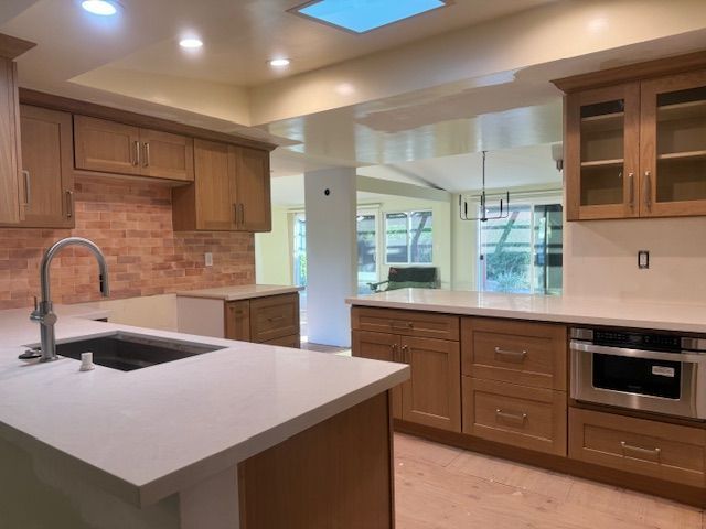 Newly renovated kitchen with light wood cabinets, white countertops, and brick backsplash.