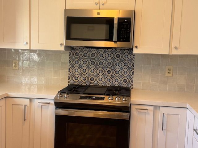 Kitchen with white cabinets, stainless steel appliances, and patterned blue and white backsplash.