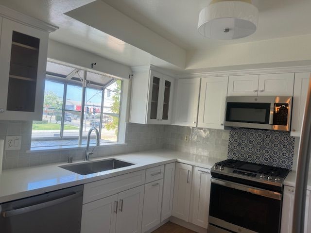 White kitchen with stainless steel appliances, white cabinets, and blue tile backsplash.