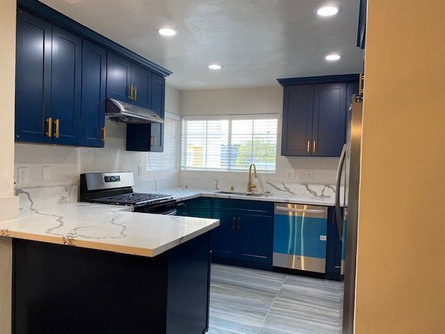 Blue kitchen with white countertops and gold hardware.