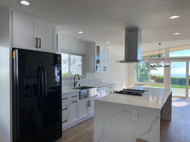 Modern white kitchen with black refrigerator, stainless steel range hood, and large island.
