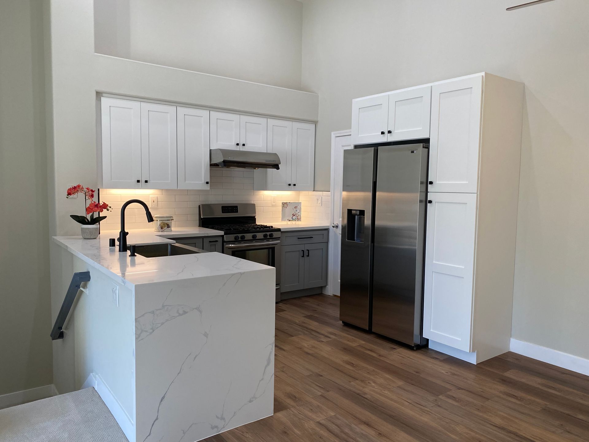 Modern kitchen with white cabinets, marble island, stainless steel appliances, and wood floors.