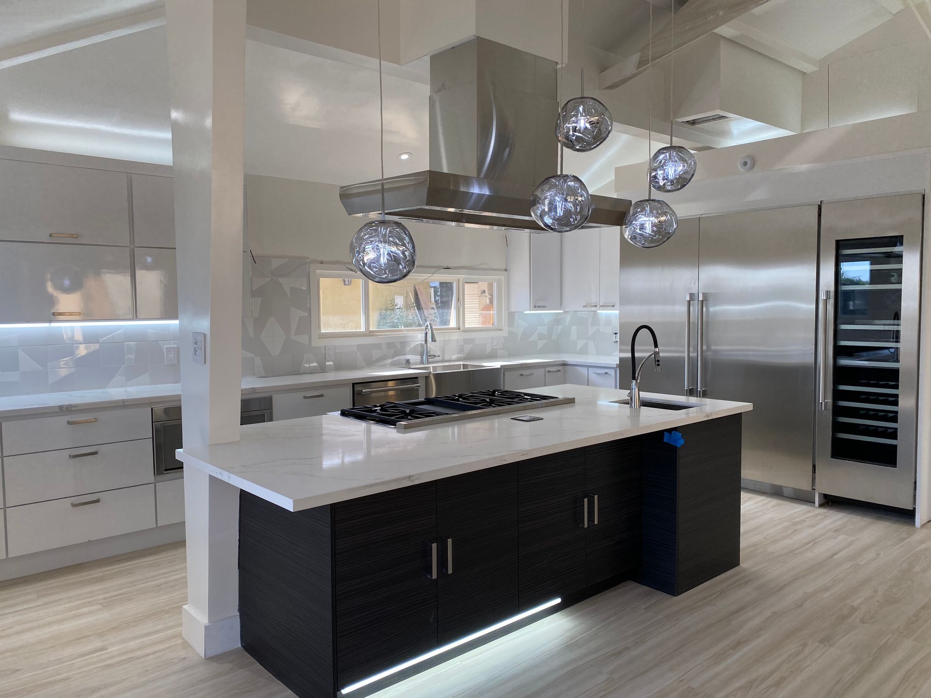 Modern kitchen featuring a white-topped island with black cabinets, stainless appliances, and hanging orb light fixtures.