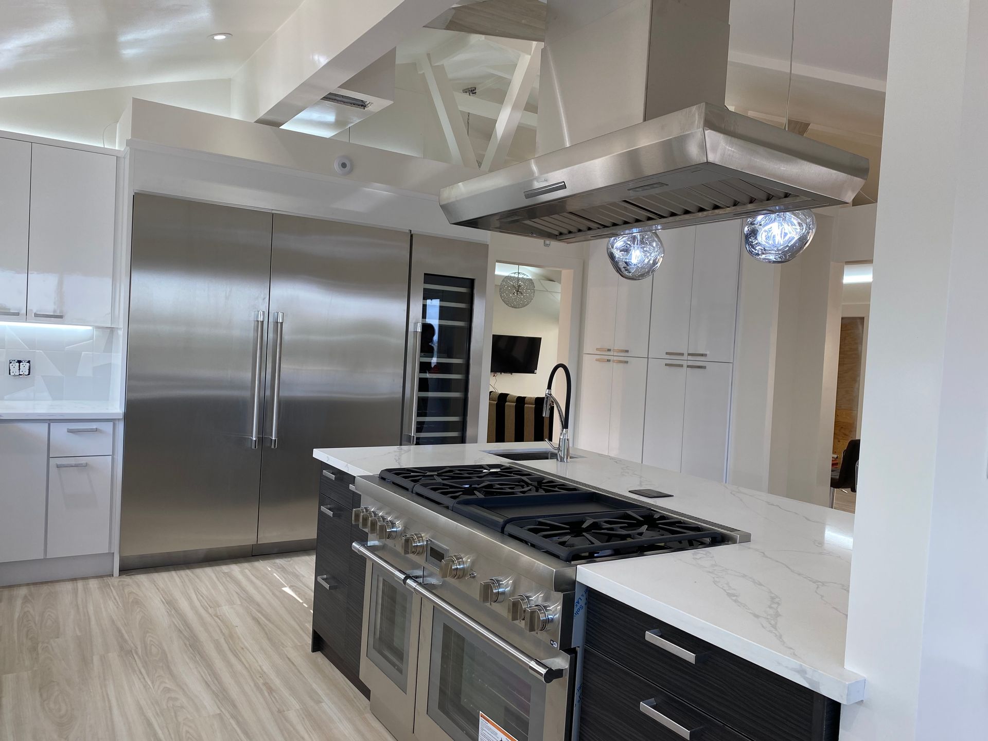 A modern kitchen features a large stainless-steel refrigerator, a gas stove island, and white countertops.