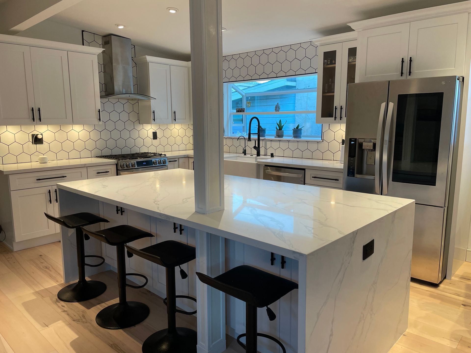 Modern white kitchen with island seating, stainless steel appliances, and geometric backsplash.
