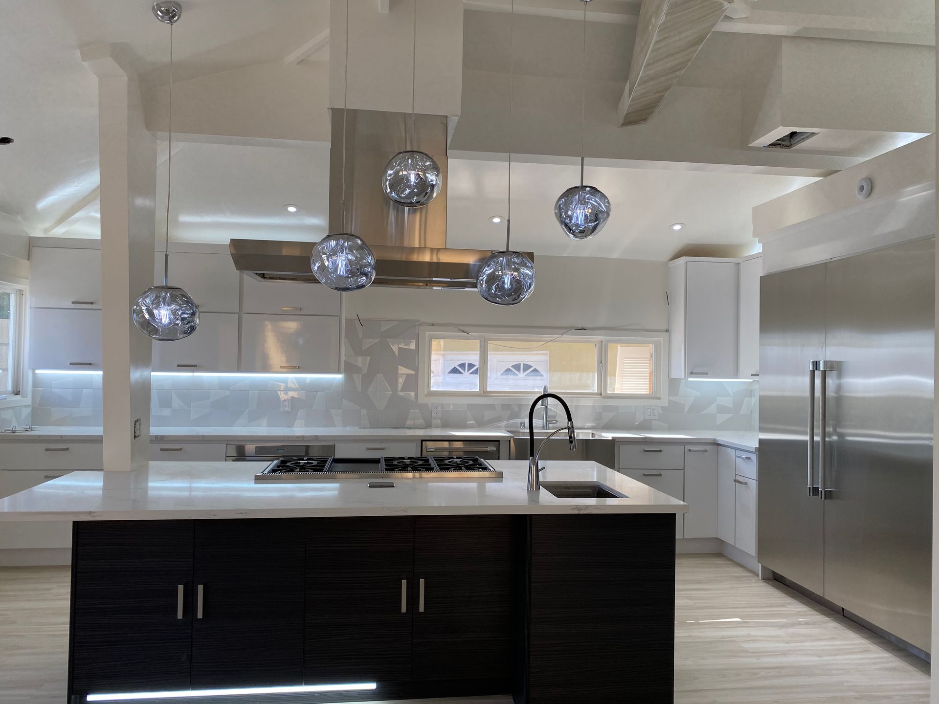 Modern kitchen with a dark wood island, white countertops, stainless steel appliances, and four hanging globe lights.