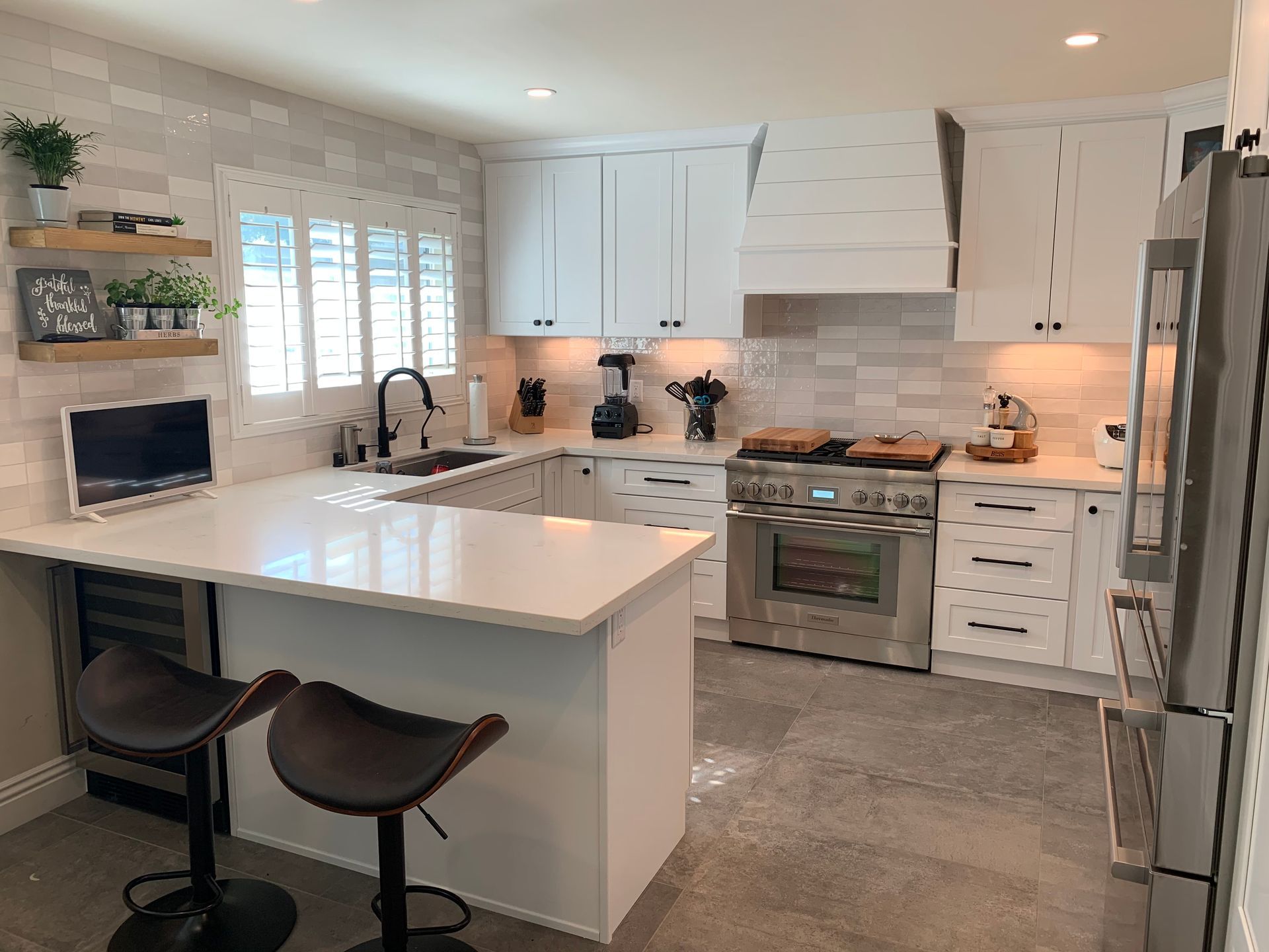 White kitchen with quartz countertops, stainless steel appliances, and two bar stools.