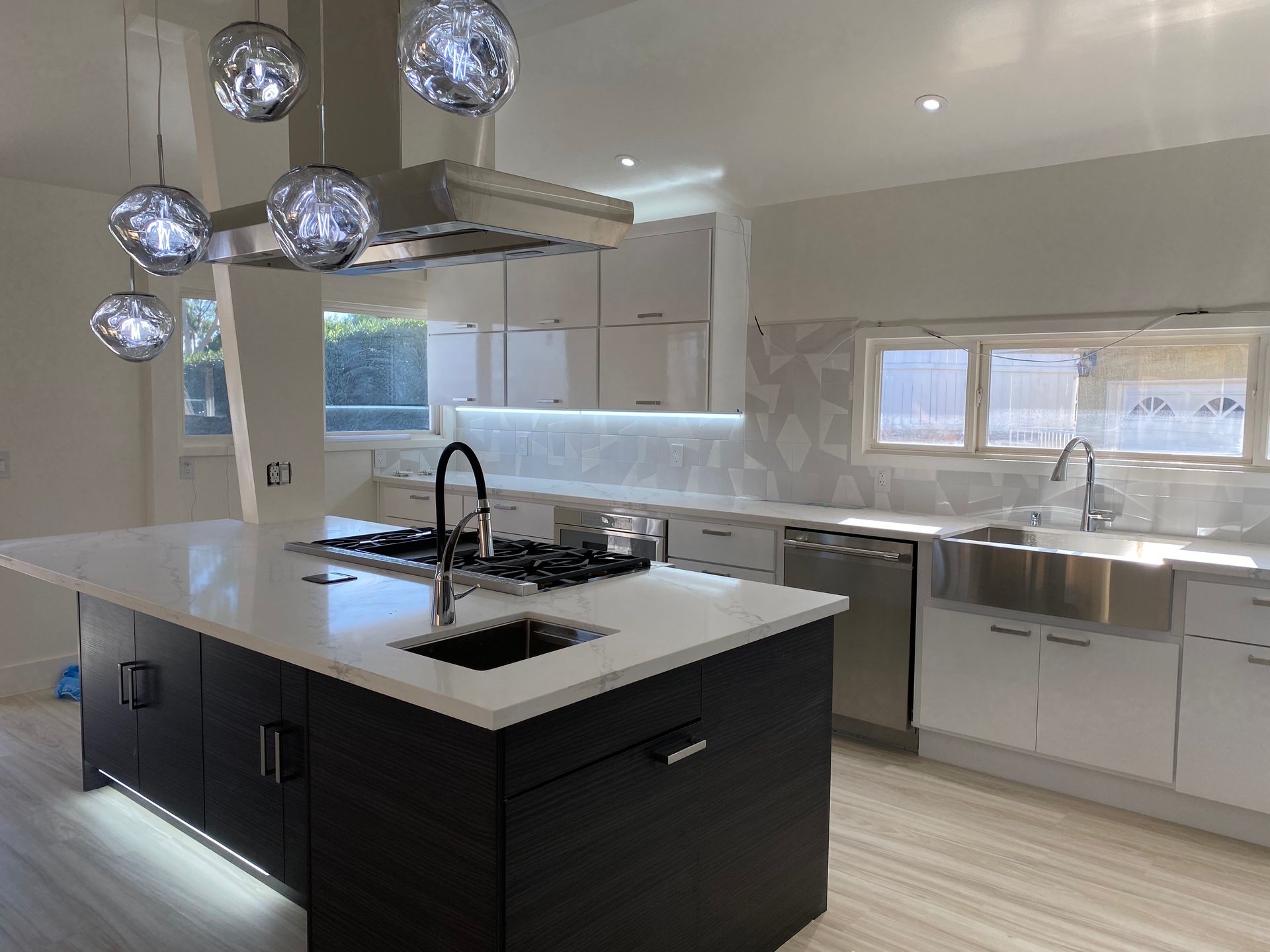 A modern kitchen with a dark-colored central island featuring a sink and cooktop, white cabinets, and spherical lights.