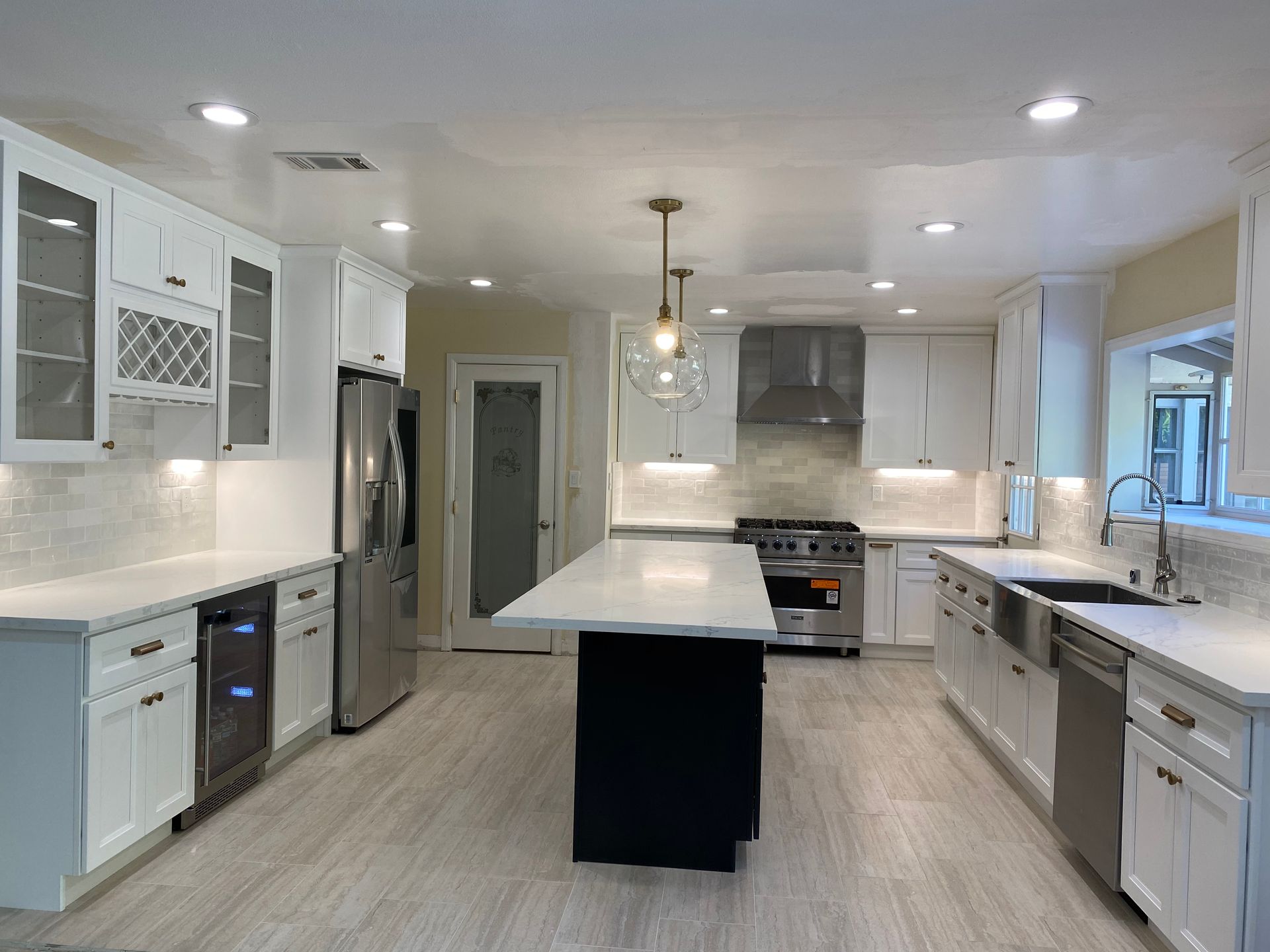 Modern white kitchen with stainless steel appliances, dark island, and light wood floors.