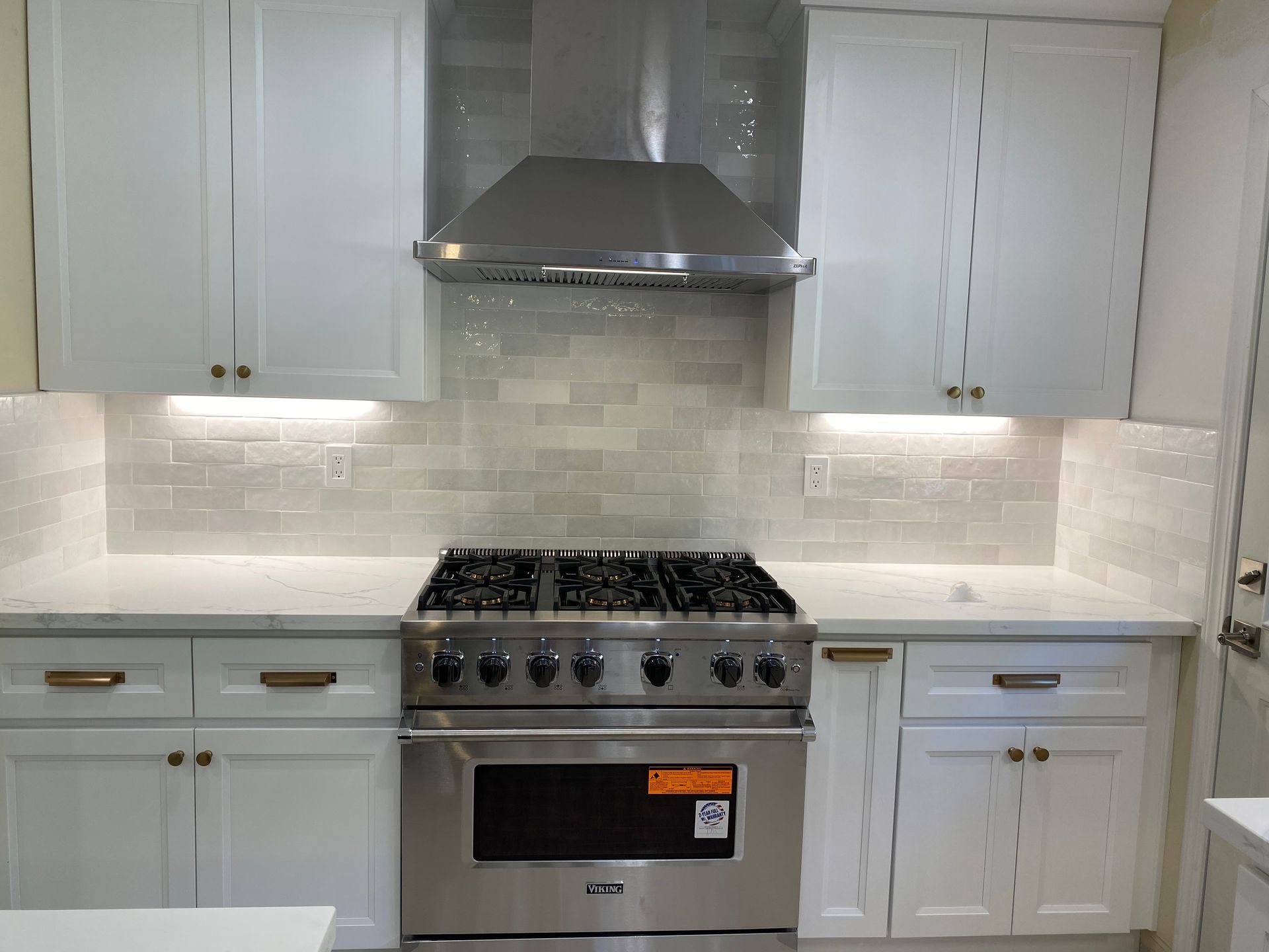 White kitchen with stainless steel stove and range hood. White cabinets and backsplash.