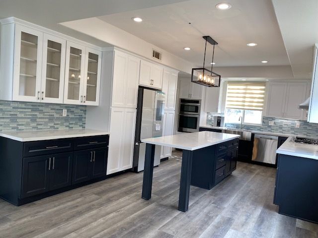 A kitchen with black cabinets, white countertops, and a large island in the middle