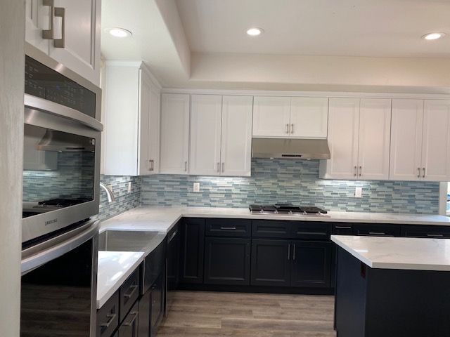 A kitchen with black bottom cabinets, white top cabinets, stainless steel appliances, and a sink
