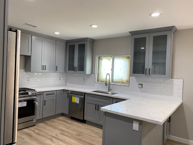 A kitchen with gray cabinets, appliances, and white countertops