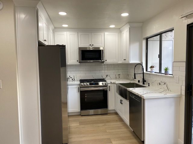 A kitchen with white cabinets, stainless steel appliances, and a sink