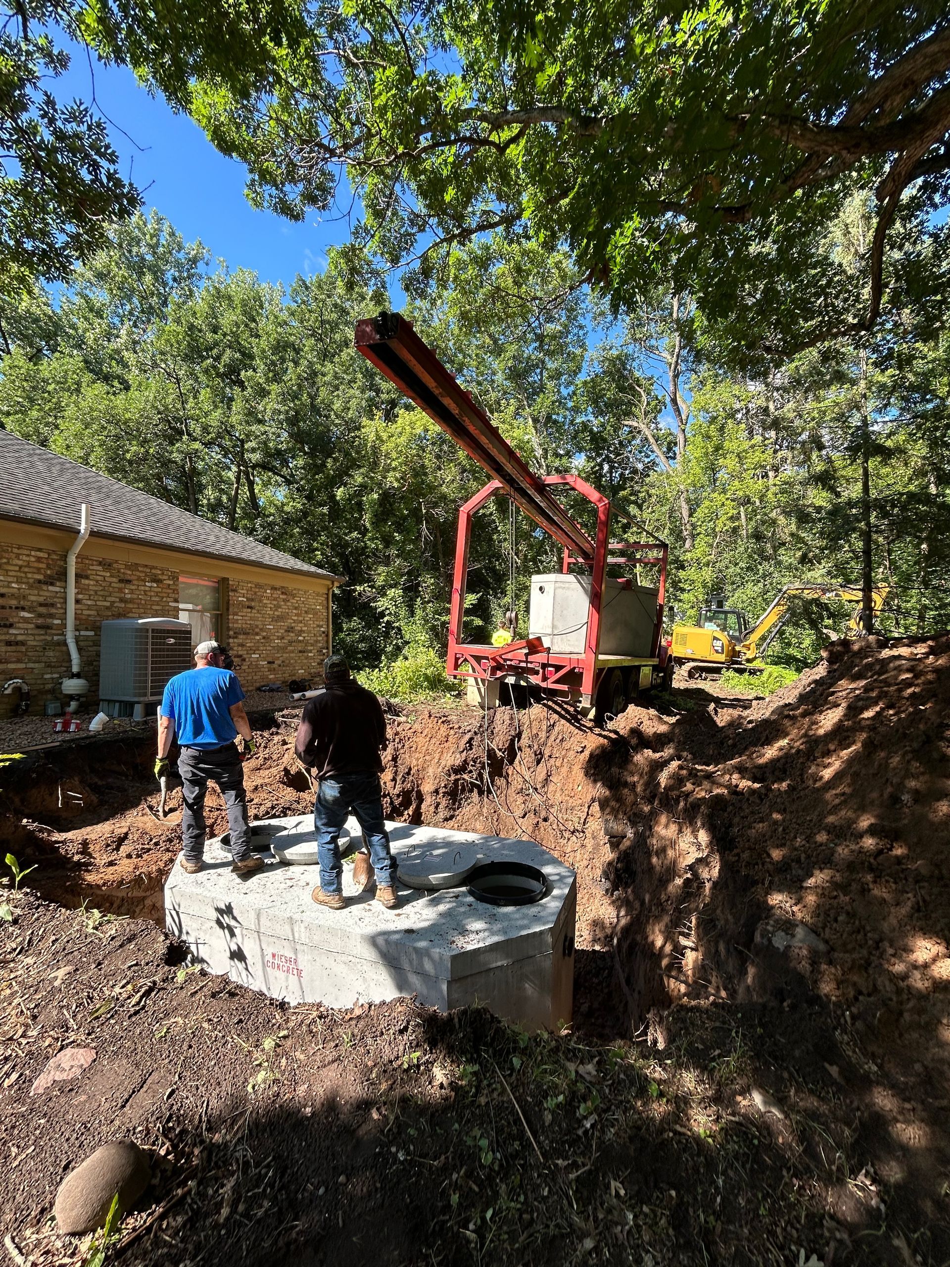 Two workers near a large concrete structure in a construction site with a crane; trees and a building in the background.