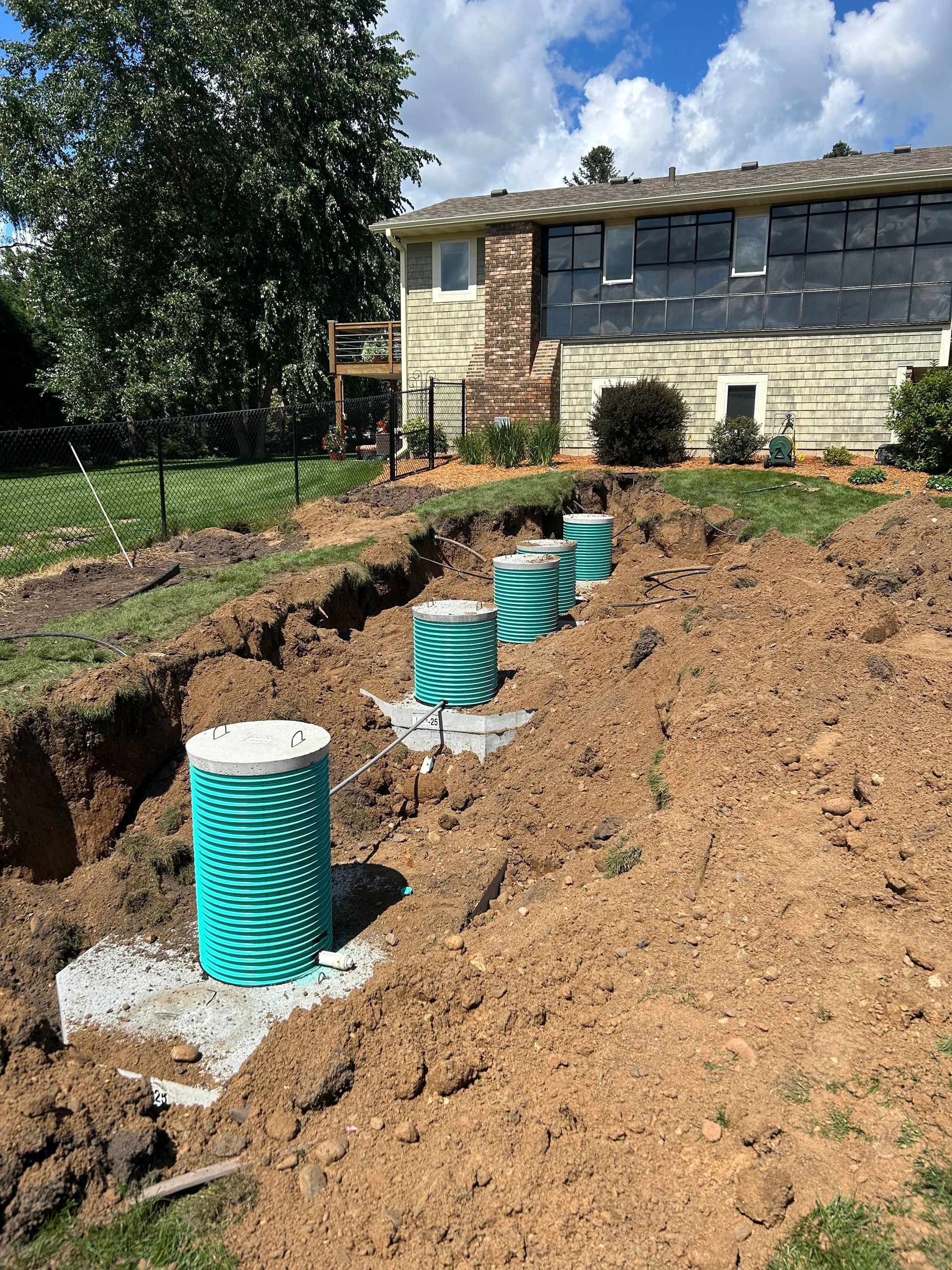 Trench with installed green septic tank components in front of a house on a sunny day.