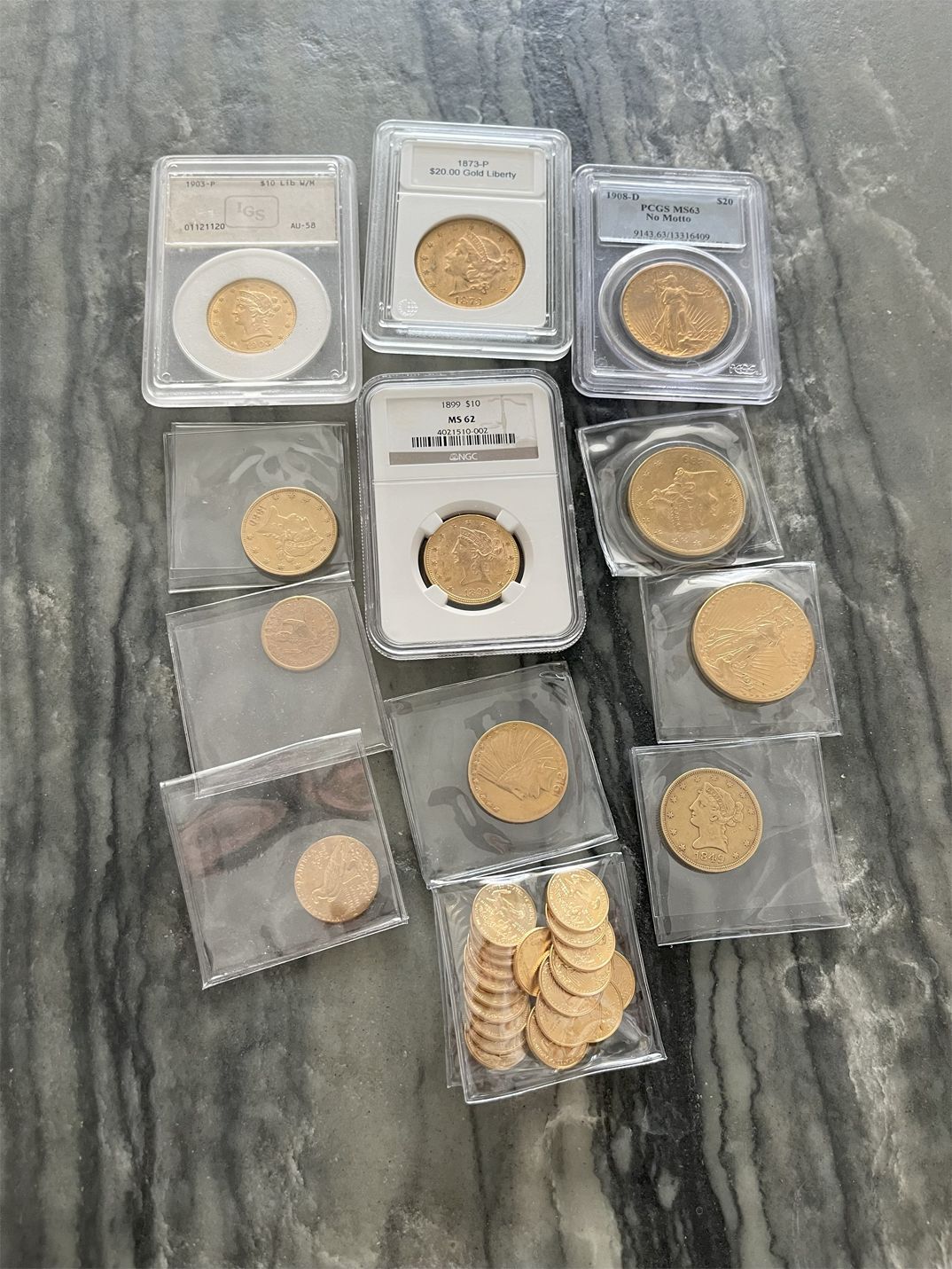 Gold coins in protective cases and plastic sleeves on a marble surface.