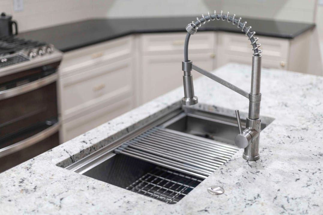 Stainless steel kitchen sink with a pull-down faucet, set in a white countertop.