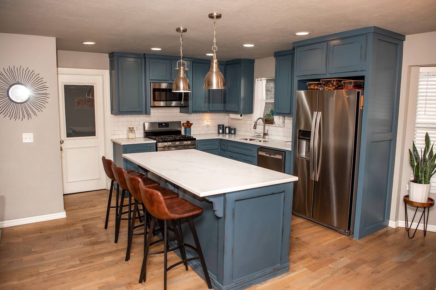 Blue kitchen with island and stainless steel appliances, wood floor, marble countertops.