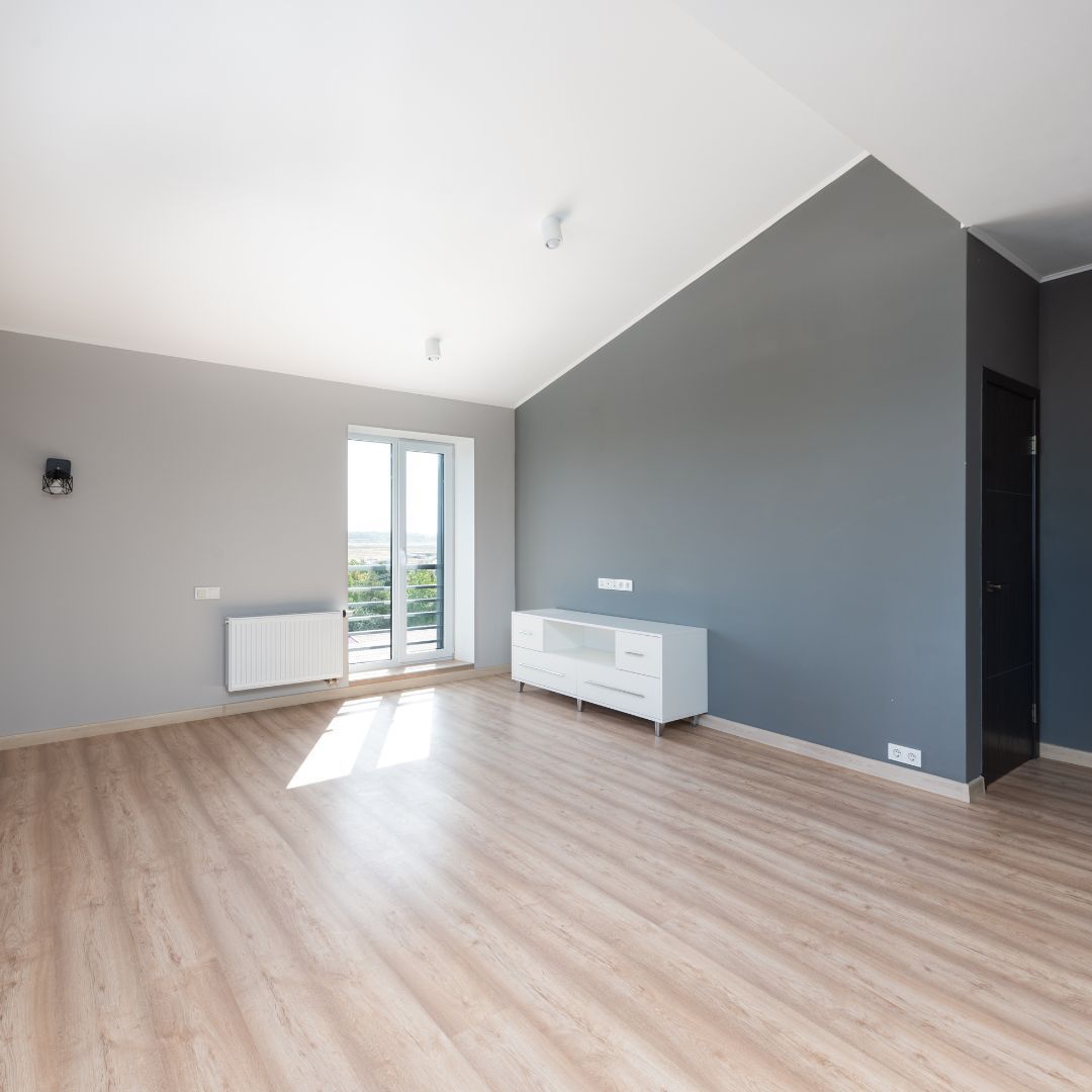 Empty modern room with gray walls, wood floor, window, white cabinet, and black door.