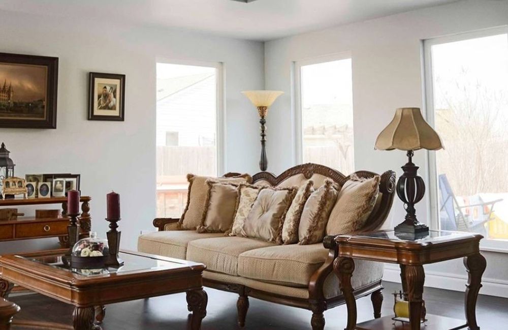 Living room with ornate furniture: sofa, side tables, coffee table, and lamps near windows.