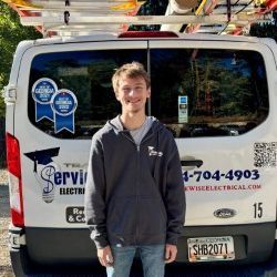 Man in a gray hoodie and cap stands in front of a ServiceWise van.