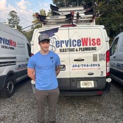 Man in a gray hoodie and cap stands in front of a ServiceWise van.